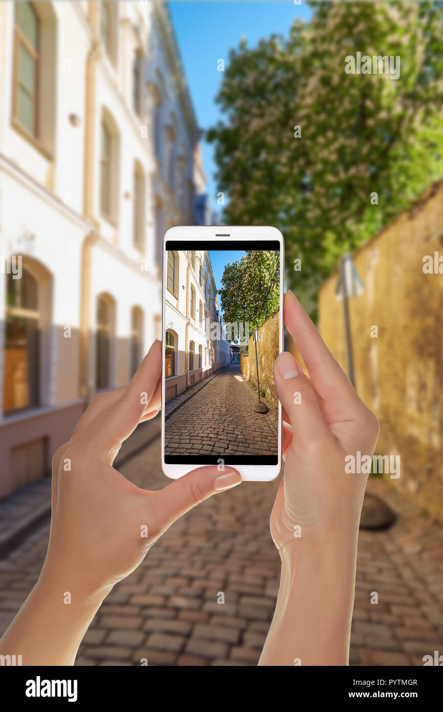 Un turista è di scattare una foto di una piccola strada europeo nella parte vecchia di Tallinn, Estonia su un telefono cellulare Foto Stock