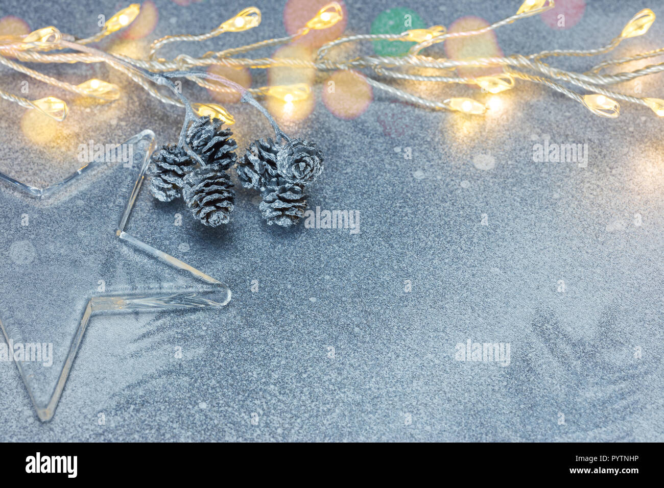 Le luci di Natale ghirlanda, stella di vetro e il ramo con i coni su sfondo argento Foto Stock