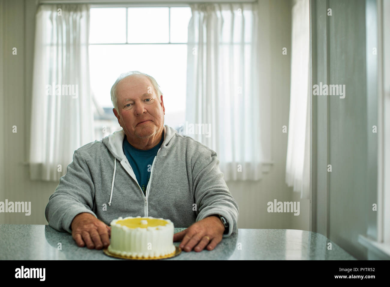 Ritratto di un anziano uomo seduto di fronte a una torta di compleanno. Foto Stock