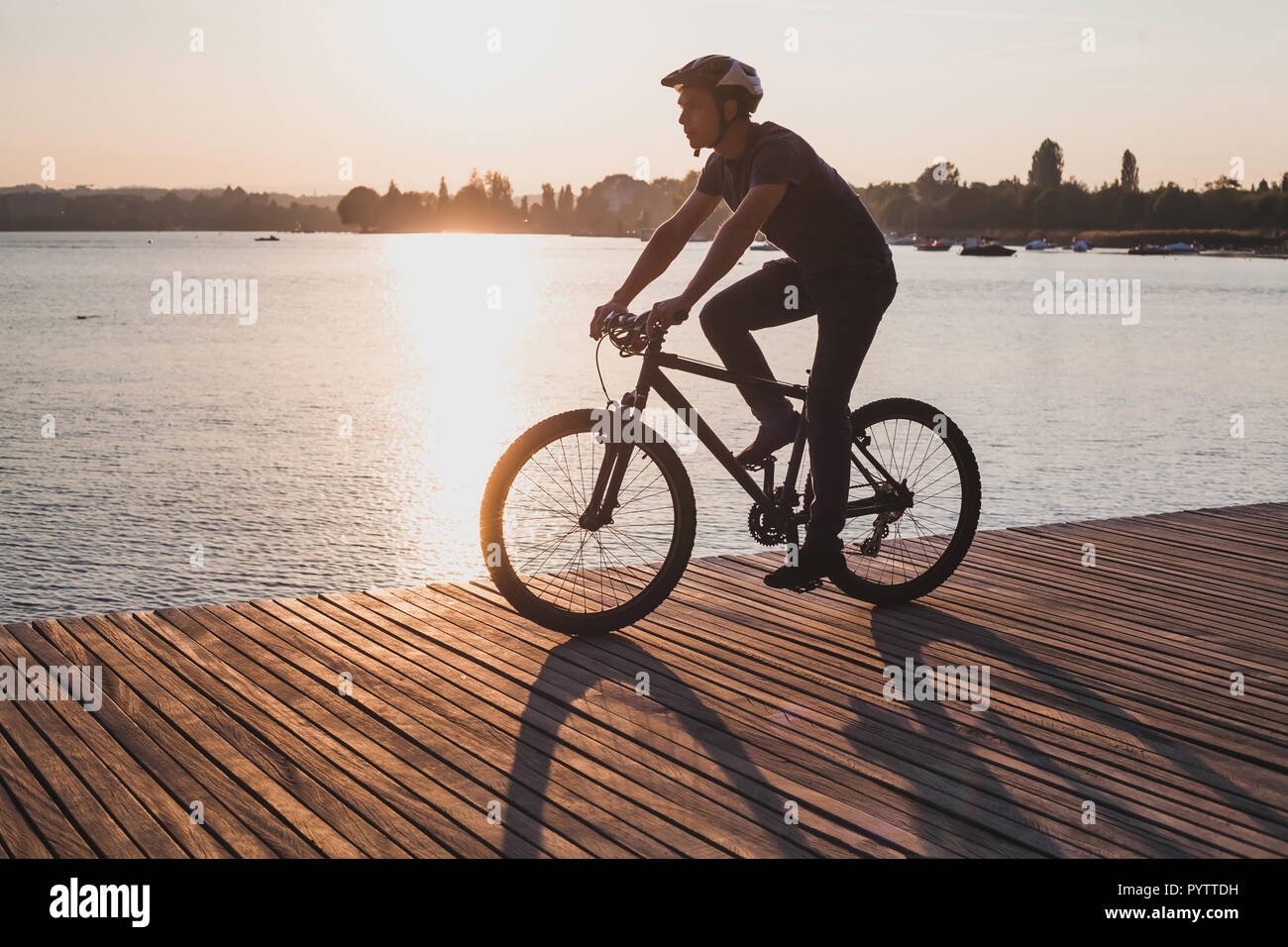 Silhouette di uomo in bicicletta in città al tramonto vicino al lago, sport ciclismo tempo libero attivo Foto Stock