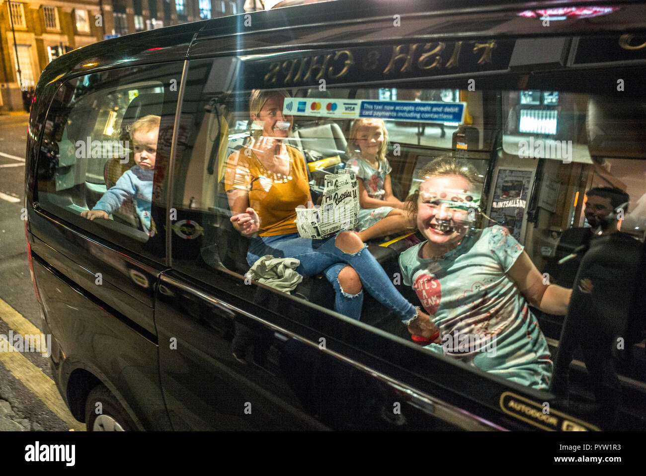 Famiglia in taxi fuori dal negozio di pesce e chip Londra. Madre e tre bambini in auto sorridendo alla macchina fotografica un bambino sembra infelice Foto Stock