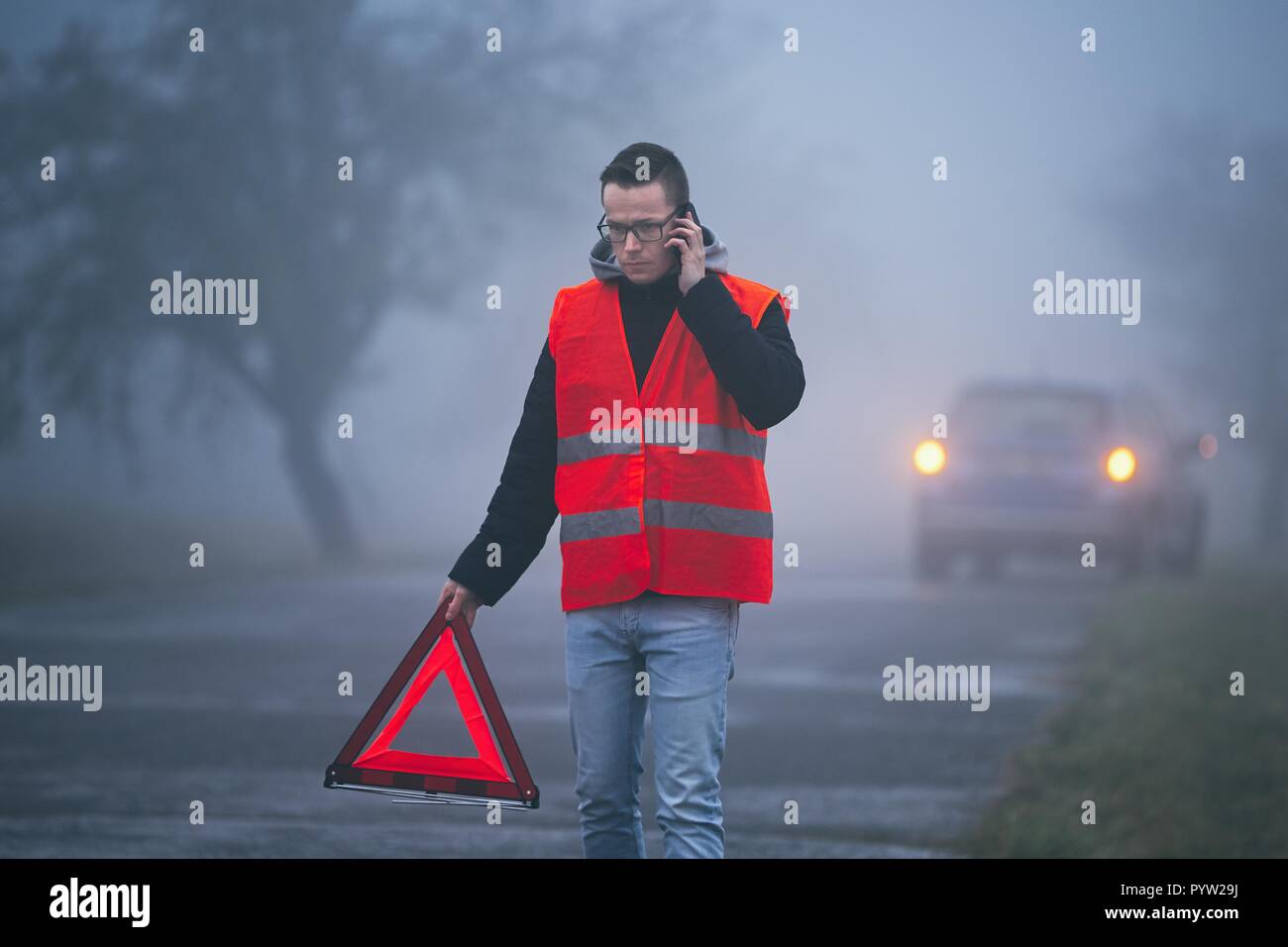 Il problema del traffico in caso di nebbia fitta. Il giovane driver di chiamata per assistenza e mettendo il triangolo di avvertenza dietro il suo Broken auto. Foto Stock