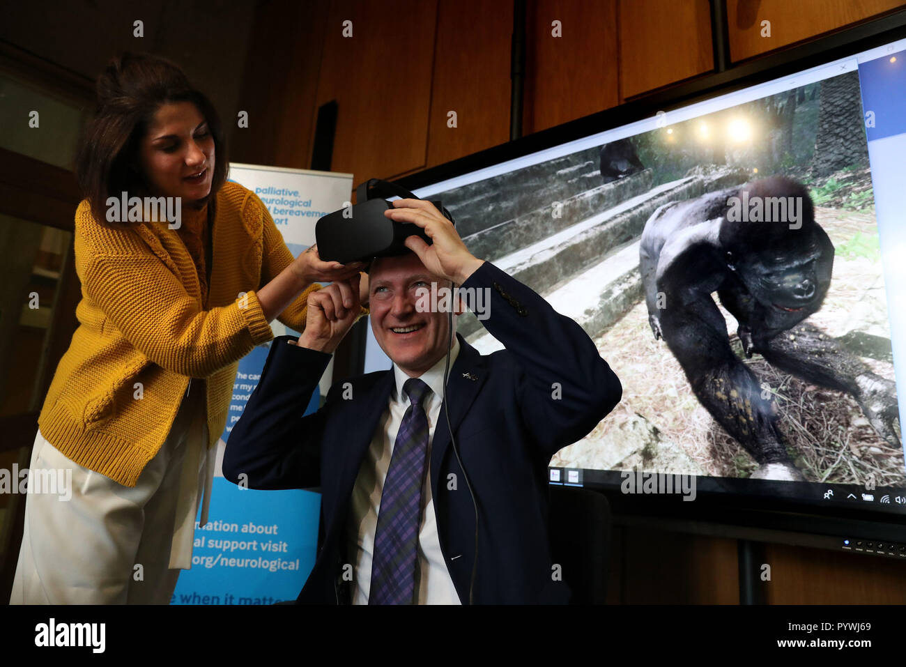 Joe FitzPatrick il Ministro per la salute pubblica, Sport e benessere con terapista ricreative Kirsty Fraser da Sue Ryder come egli tenta di eseguire una realtà virtuale di esperienze al Parlamento scozzese a un evento in fase di esecuzione da Lewis Macdonald MSP in aiuto delle Sue Ryder della carità che opera Dee Visualizza corte - uno specialista neurologiche centro di cura di Aberdeen. Foto Stock