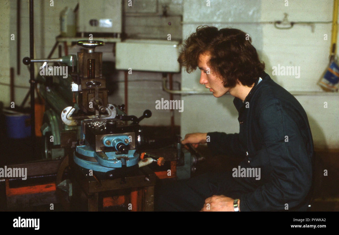 Anni Settanta, storico, un giovane maschio engineering apprendista indossando tute di seduta all'interno di un workshop facendo lamiera usando un tornio, Inghilterra, Regno Unito. Foto Stock