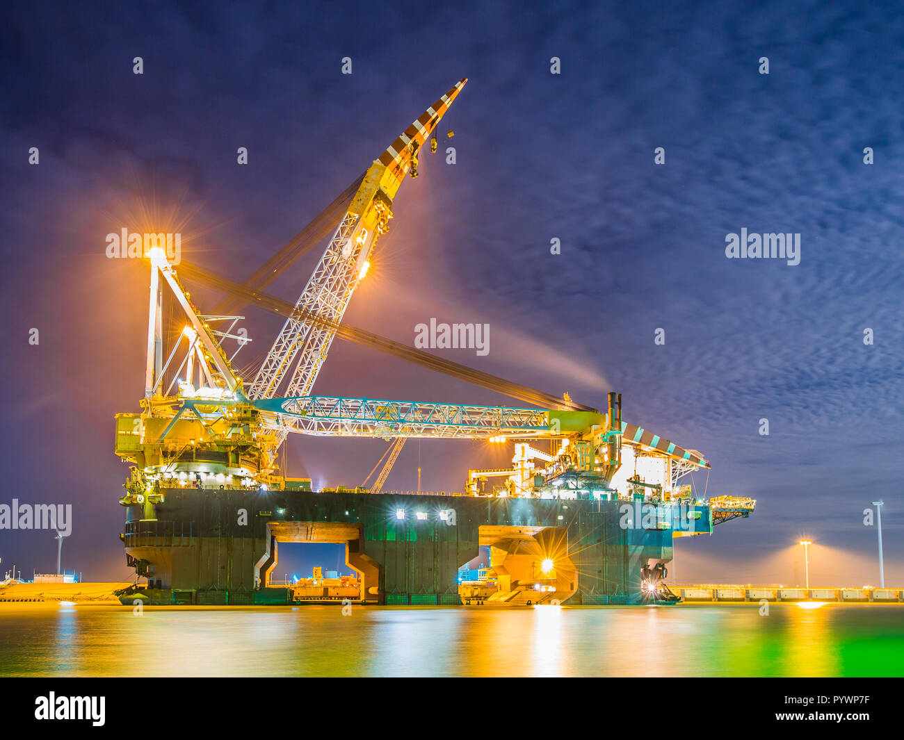 Enorme Pipelay Crane nave ormeggiata in un porto e illuminato da luci al tramonto Foto Stock