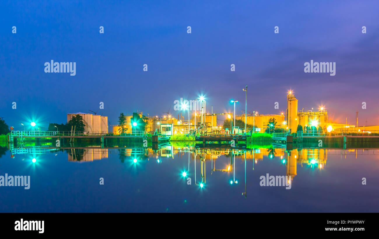 Luci di un sito di docking riflettendo in acqua a una piccola raffineria di petrolio in una sostanza chimica area industriale nel crepuscolo Foto Stock