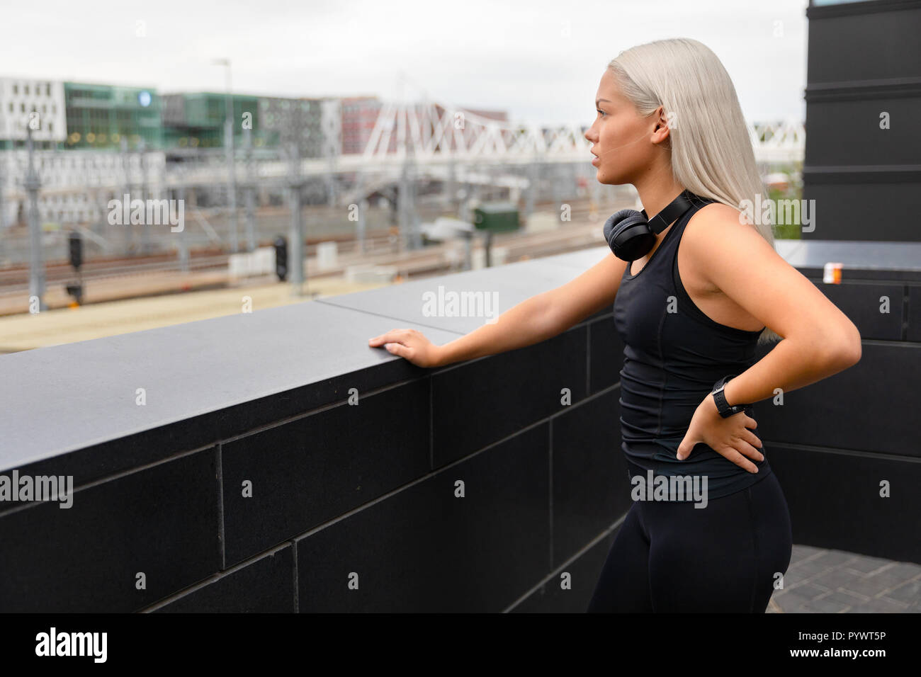Montare atleta femminile con le cuffie e Smartwatch riposa dopo allenamento sul ponte Foto Stock