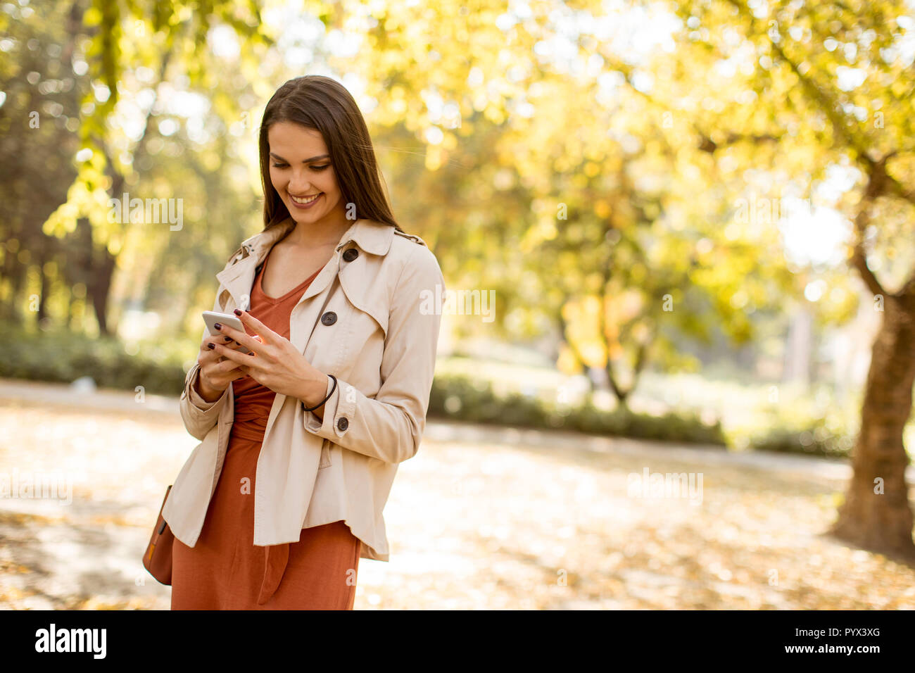 Felice giovane donna utilizzando il cellulare in autunno parco sulla bella giornata Foto Stock