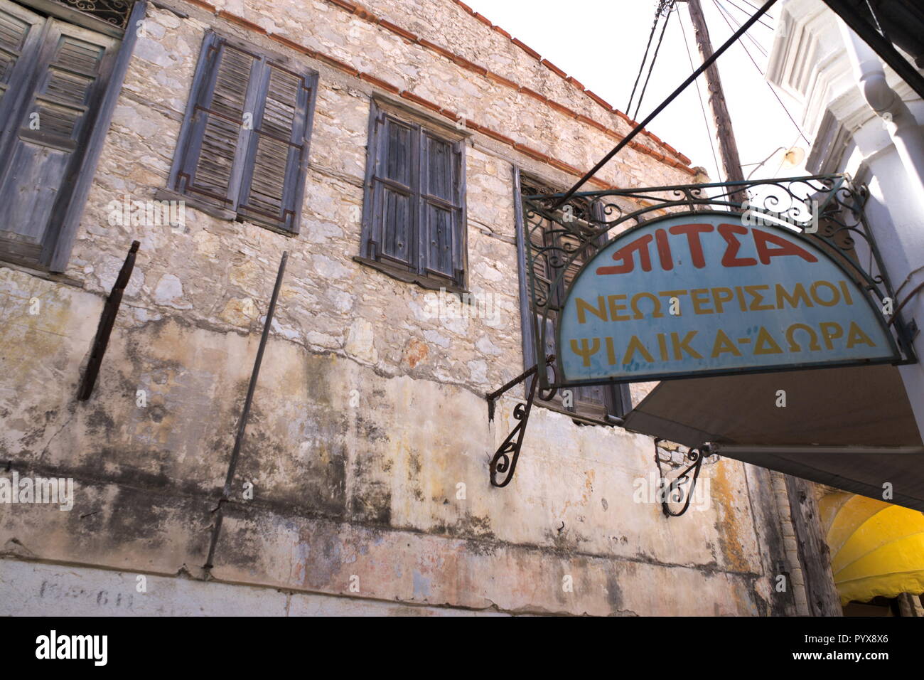 Vista di vecchi edifici nella splendida isola greca di Symi. Un segno di pubblicità vecchio stile in un elegante telaio di metallo, e un edificio vecchio e semplice Foto Stock