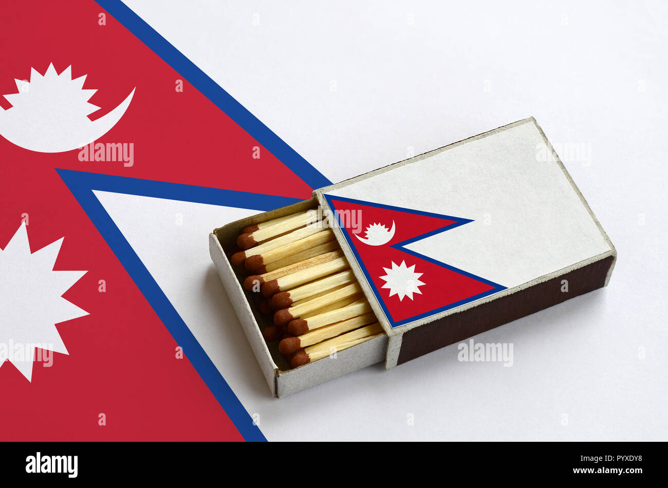 Il Nepal flag è mostrato in un aperto la scatola di fiammiferi, il quale è riempito con corrispondenze e giace su di una bandiera di grandi dimensioni. Foto Stock