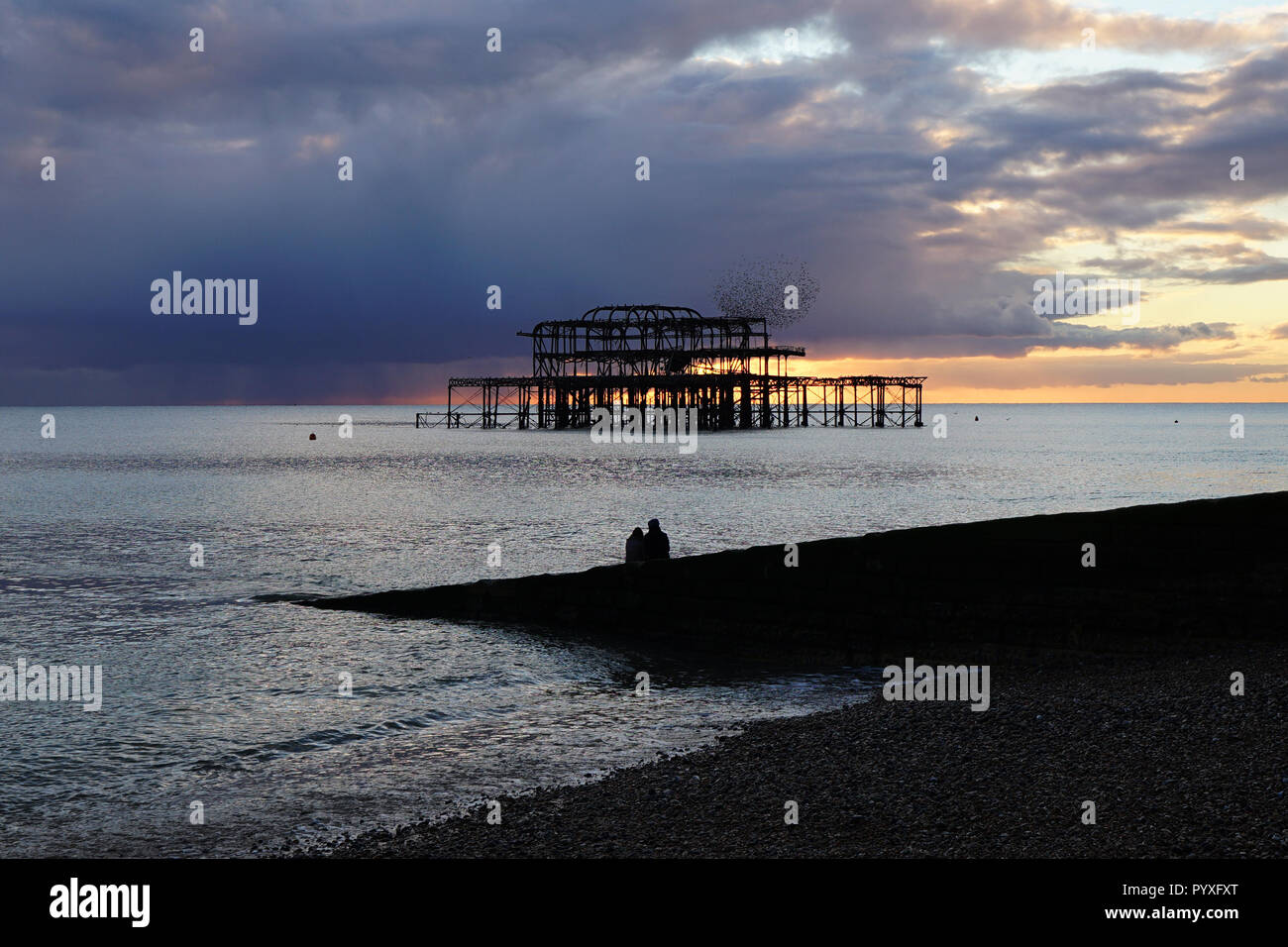 West Pier di Brighton al tramonto, con una romantica coppia che si staglia contro le rovine e una murazione di uccelli Foto Stock
