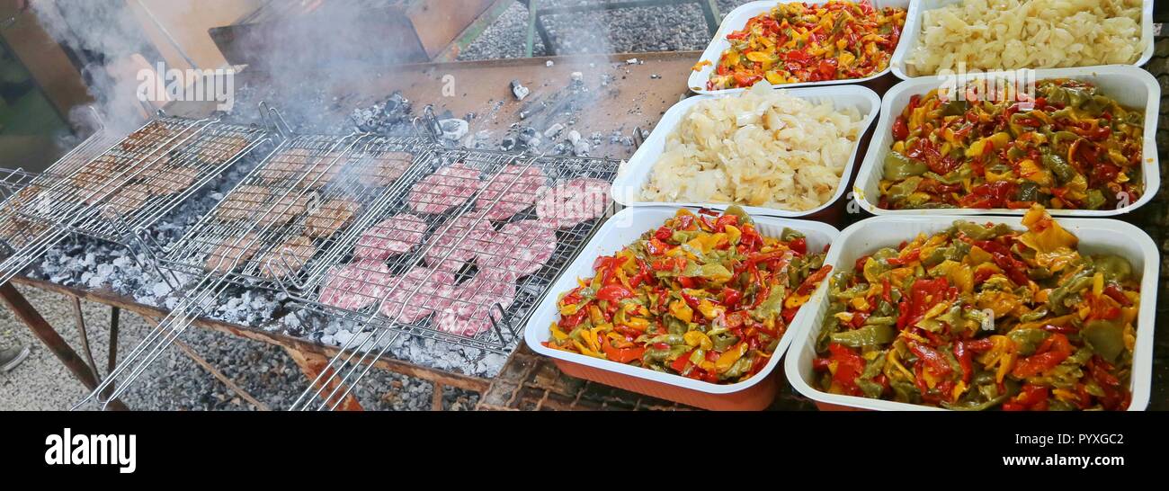 Vaschette di peperoni e cipolle vicino grigliate con molti hamburger cotto per un festival Foto Stock