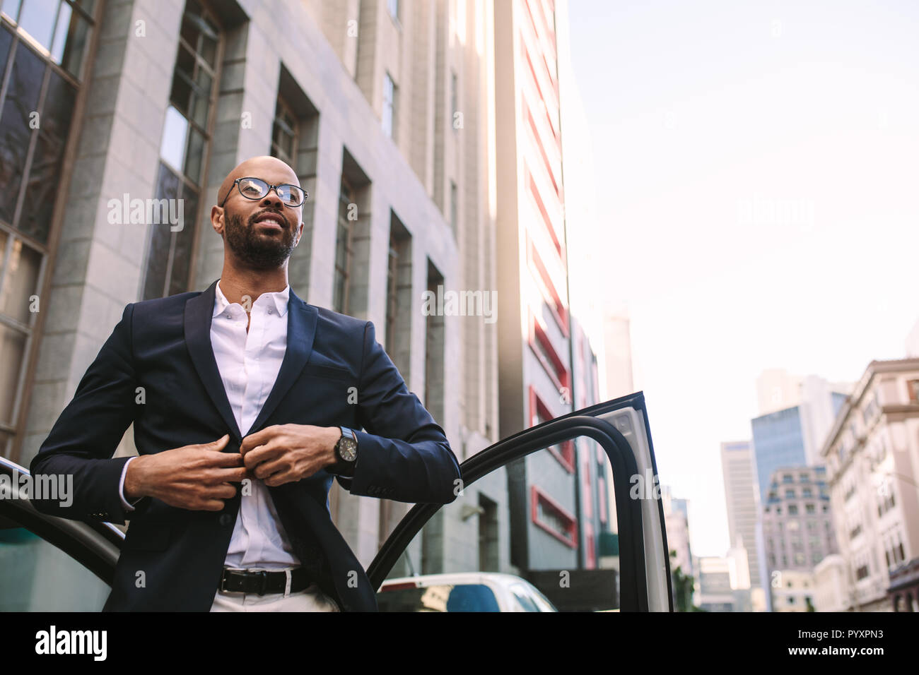 Ritratto di un bel giovane imprenditore di scendere dalla vettura sulla strada e abbottonatura la sua giacca. African uomo in piedi con la sua auto in città. Foto Stock