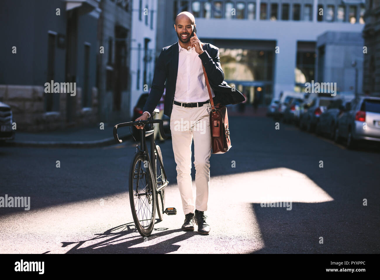 Ritratto di African uomo a camminare con la bicicletta per lavoro e parlando al telefono. Uomo d'affari andare in ufficio con la sua moto. Foto Stock