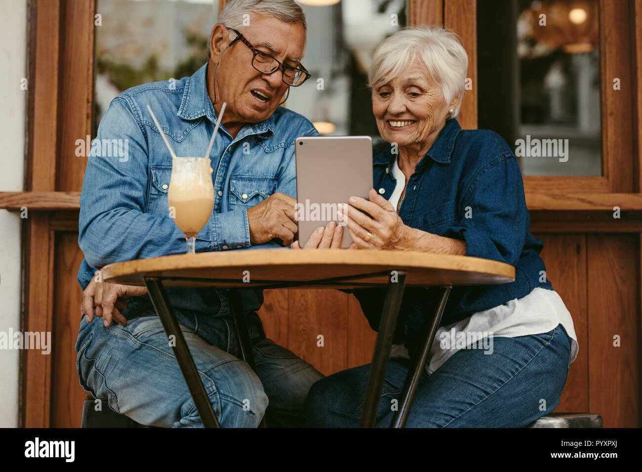 Felice coppia in pensione seduto presso la caffetteria e utilizzando digitale compressa. Il vecchio uomo e donna con tablet pc al cafe. Foto Stock