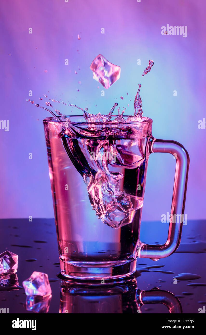 Gli spruzzi d'acqua. La caduta di cubetti di ghiaccio in un bicchiere di acqua su uno sfondo colorato Foto Stock