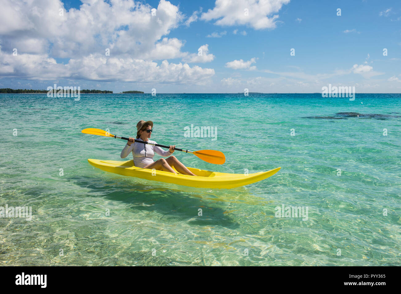 Turista femminile kayak nelle acque turchesi di Tikehau, Arcipelago Tuamotu, Polinesia Francese Foto Stock