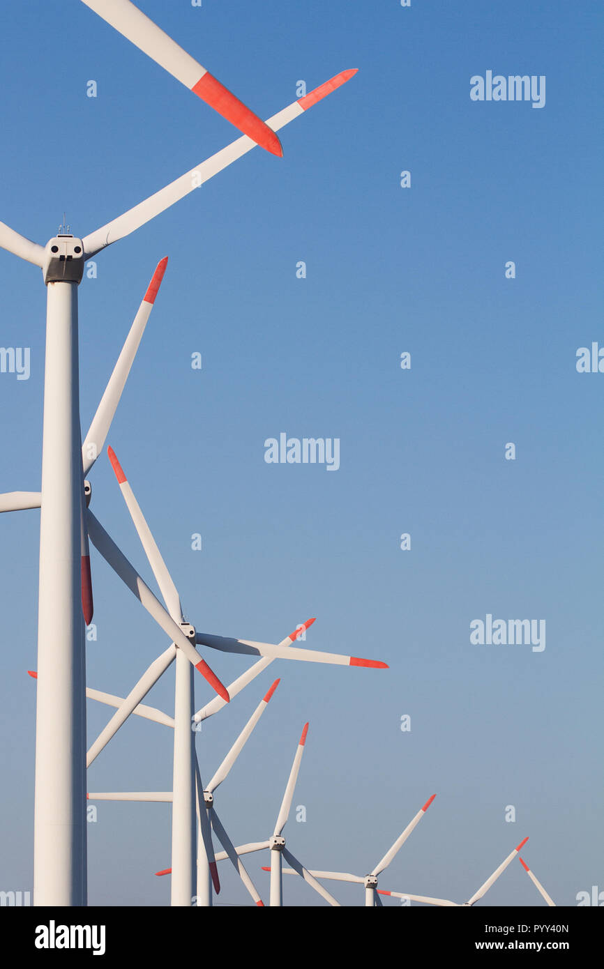 Verticale vista anteriore della fila white eolian turbine eoliche in una fattoria di energia contro un cielo blu chiaro con copyspace Foto Stock