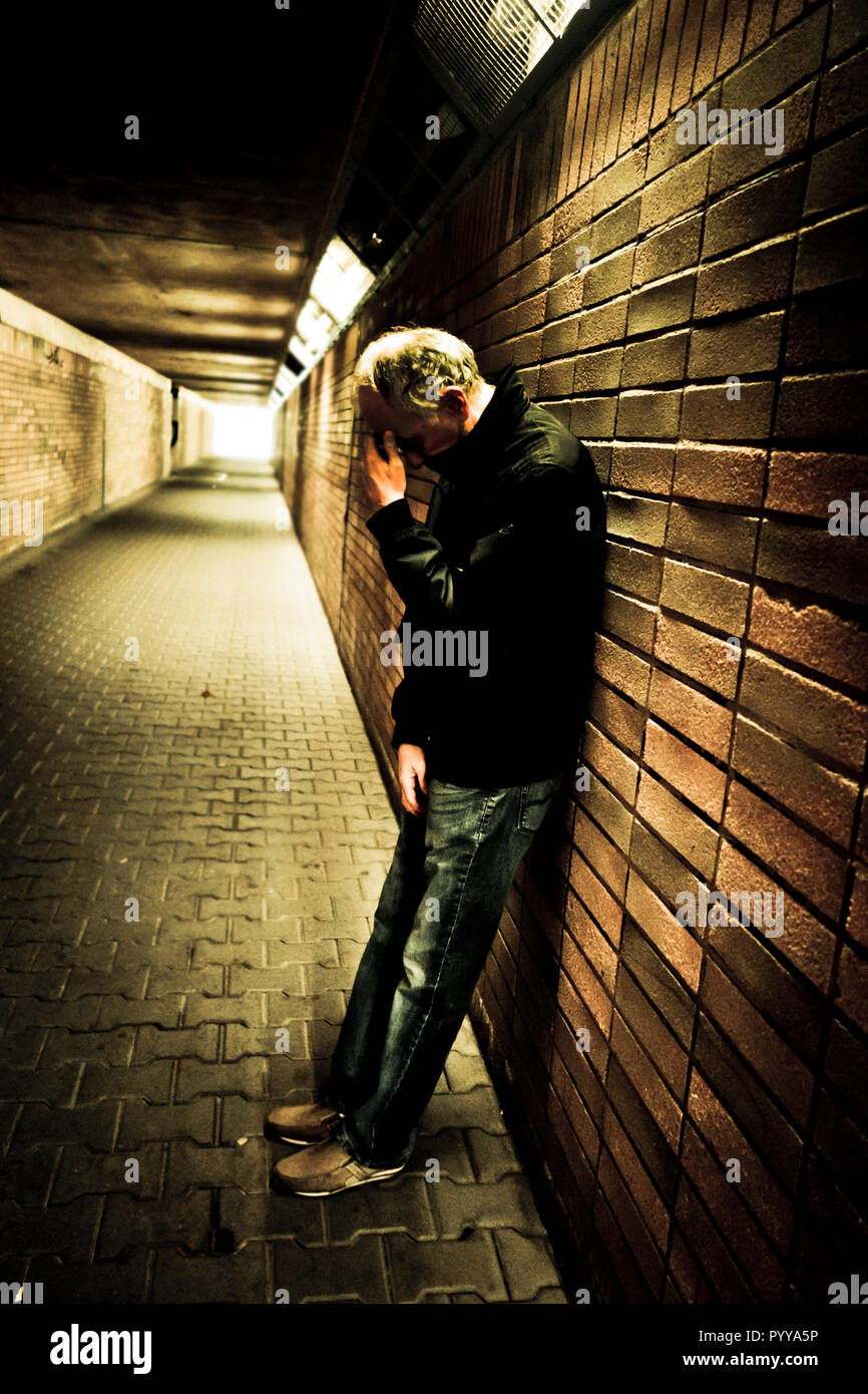 Uomo appoggiato a un muro in un sottopassaggio, soli e tristi, mano della sua testa . Concetto di depressione Foto Stock