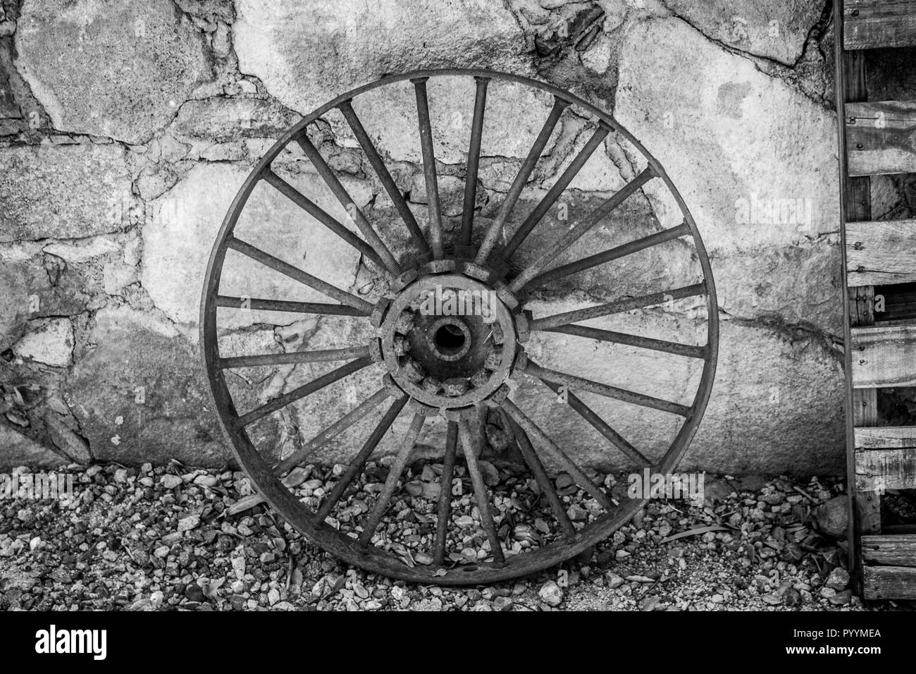 Acciaio antiche ruote a raggi e pallet in legno appoggiata contro un muro di pietra sullo sfondo Foto Stock