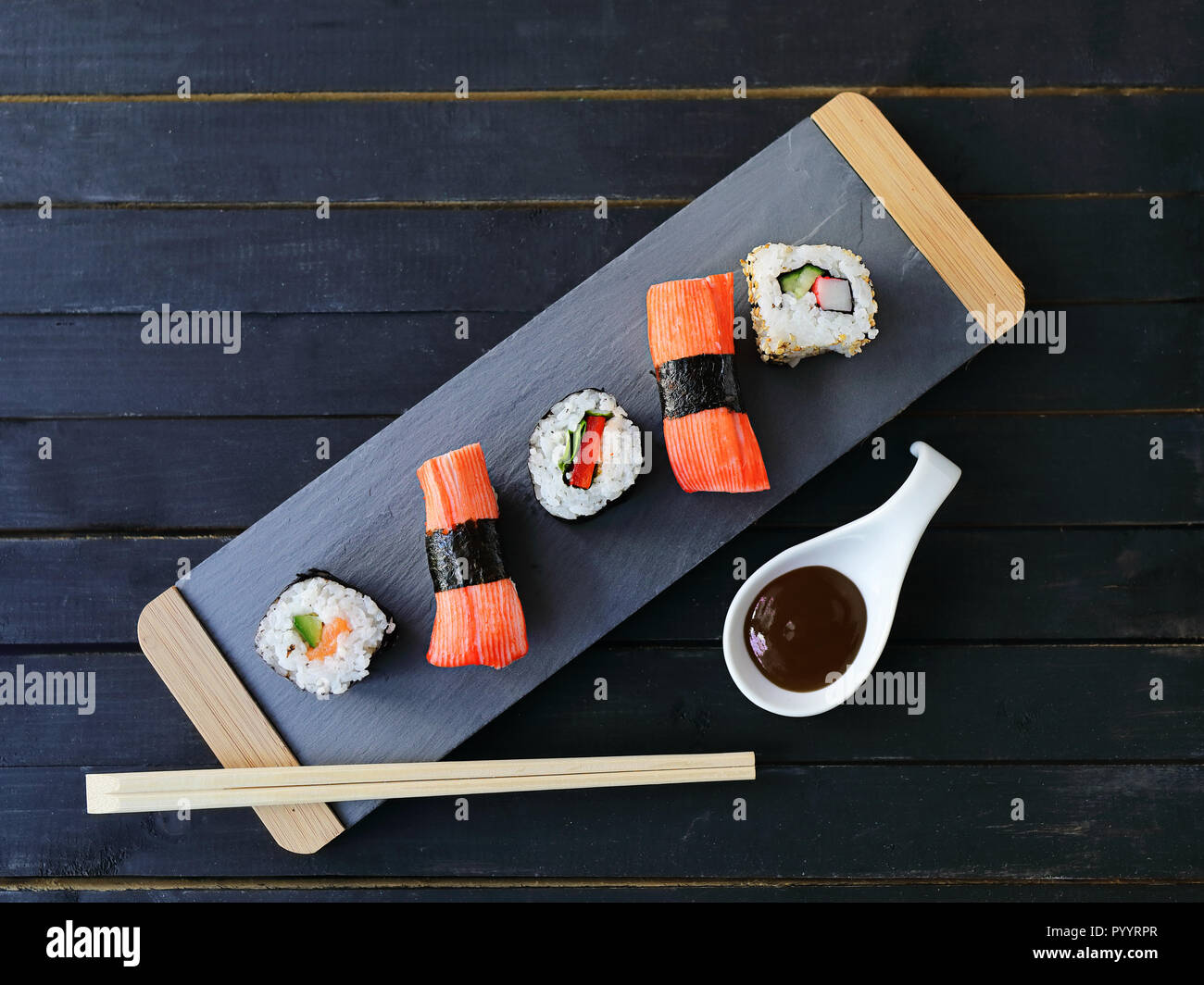 Scheda di presentazione di sushi con riso e salmone e panini con tonno e salsa piccante al buio su un sfondo di legno,. Il cibo giapponese di stile. Vista superiore Foto Stock
