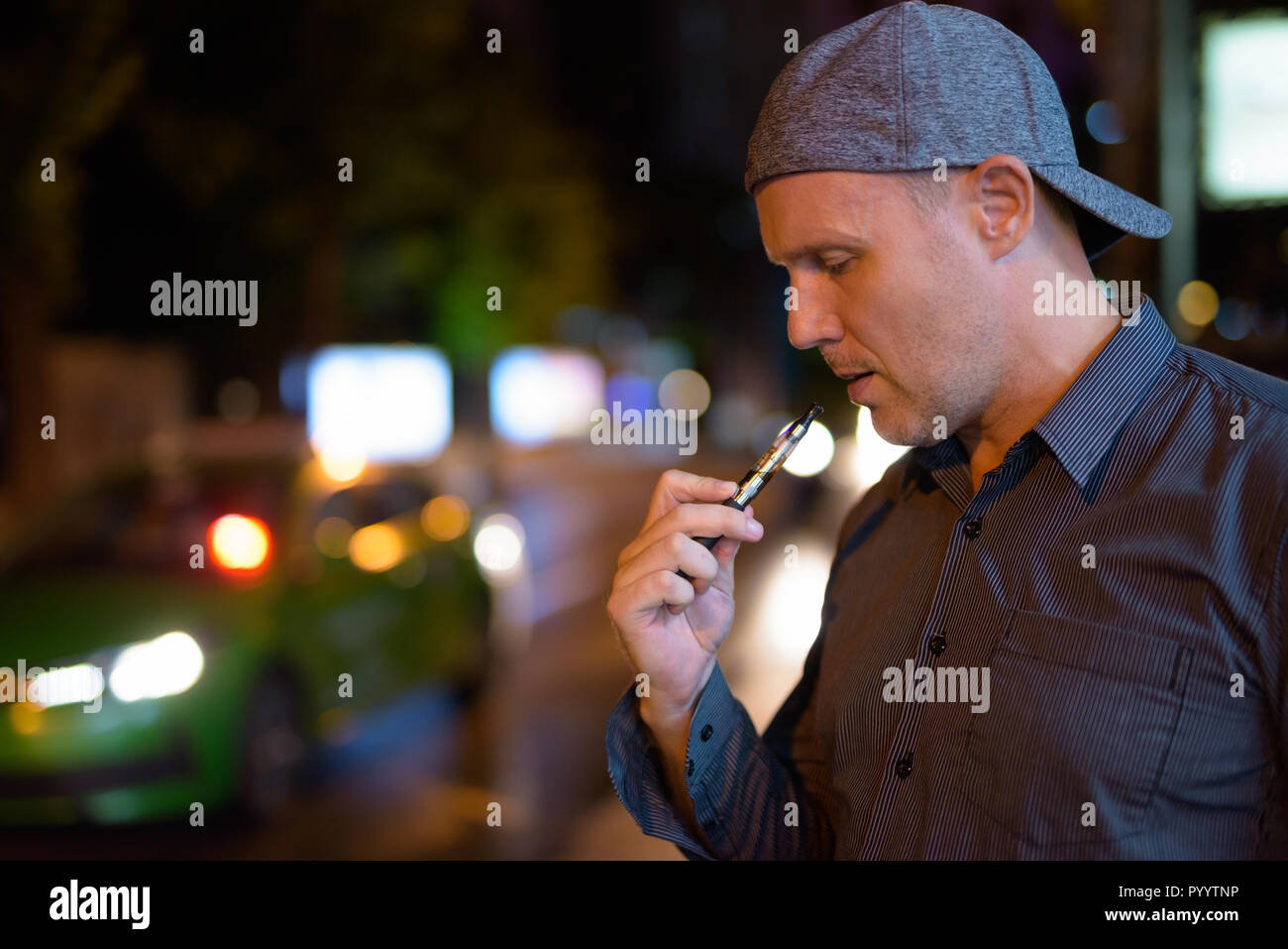 Uomo maturo di fumare sigarette elettroniche per le strade di notte Foto Stock