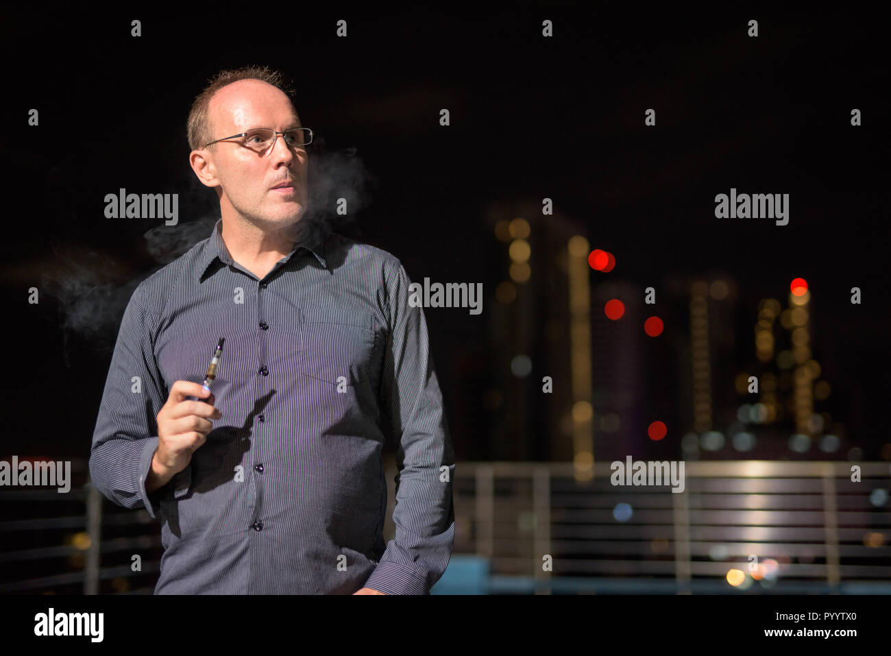 Uomo maturo di fumare sigaretta elettronica sulla piscina sul tetto Foto Stock