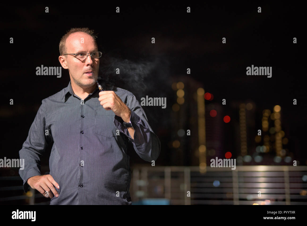 Uomo maturo di fumare sigaretta elettronica sulla piscina sul tetto Foto Stock