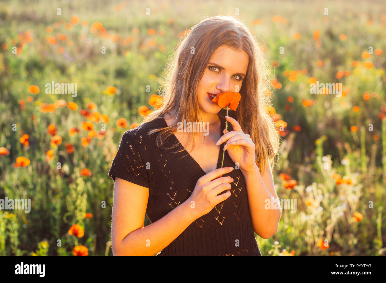 Bella ragazza nel campo sniffing fiore di papavero Foto Stock