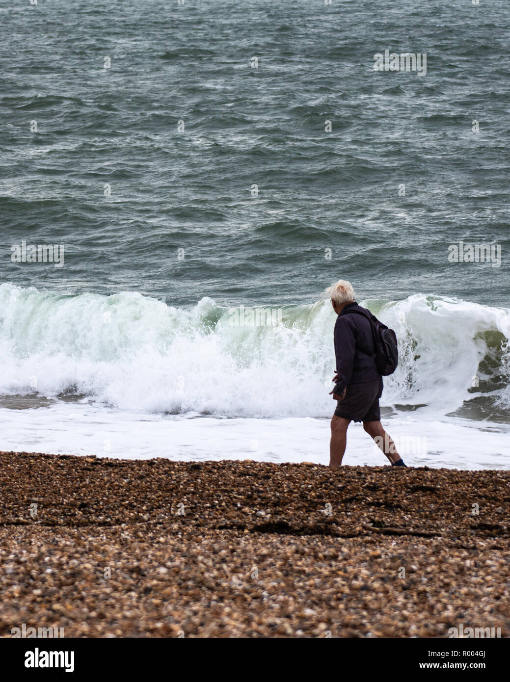Un uomo di mezza età camminare da solo su una spiaggia di ciottoli durante le tempeste Foto Stock