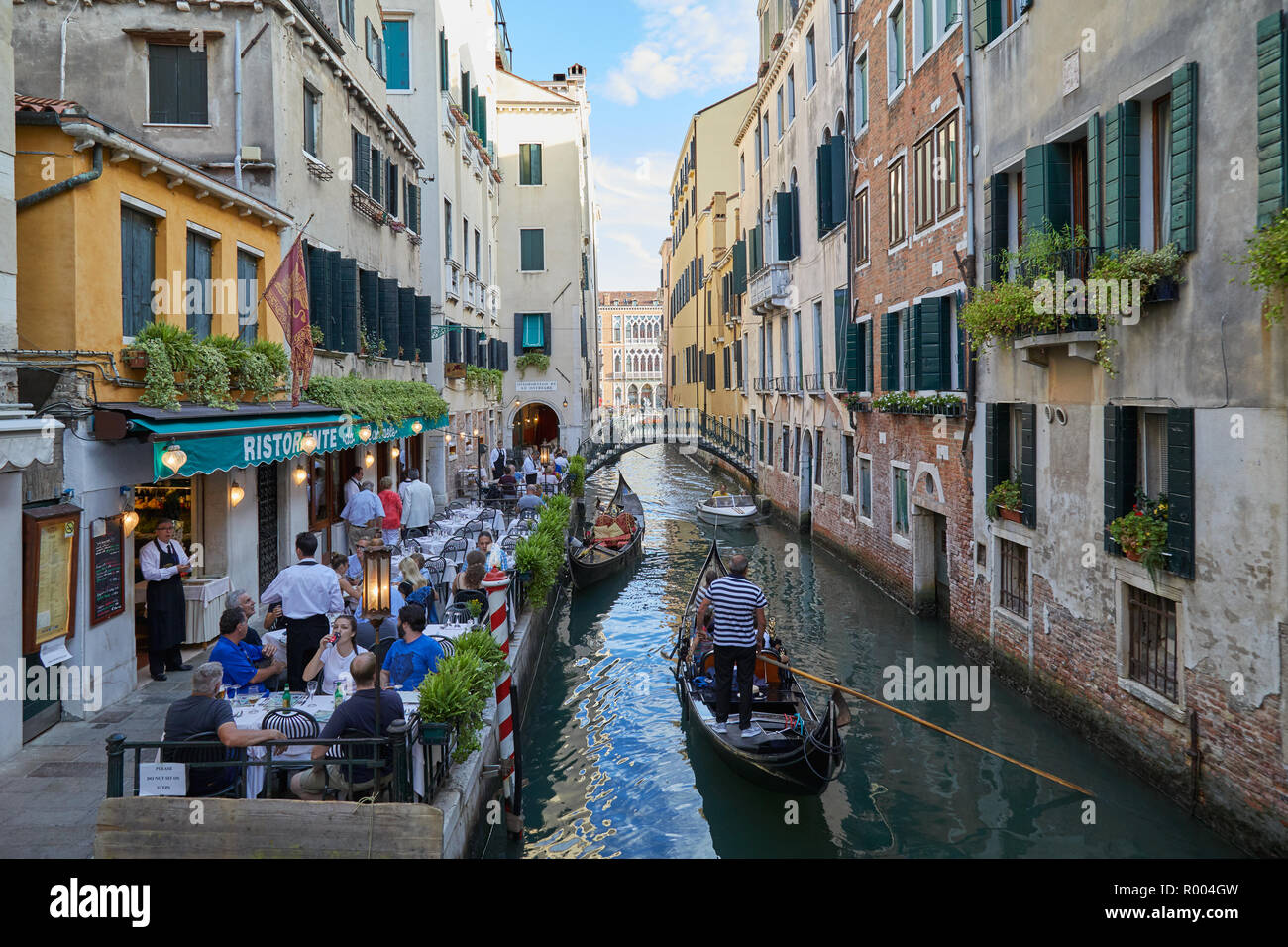 Venezia, Italia - 13 agosto 2017: ristorante con tavoli sul marciapiede con persone a cena e gondola passando nel canale Foto Stock