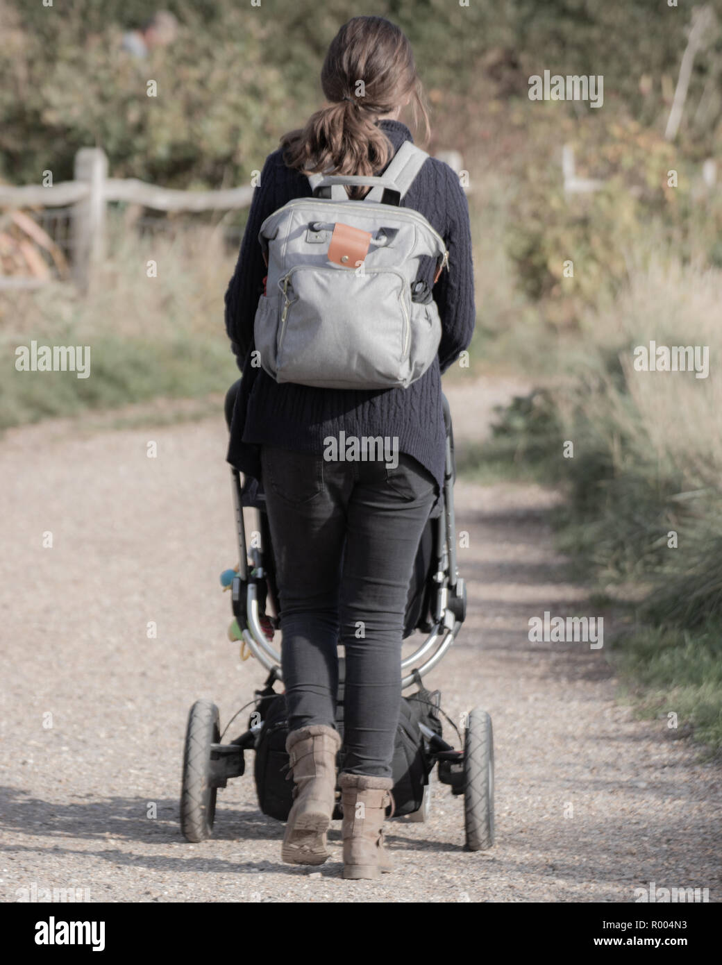 Una madre indossa uno zaino di spingere un passeggino o carrozzina su un percorso di paese Foto Stock