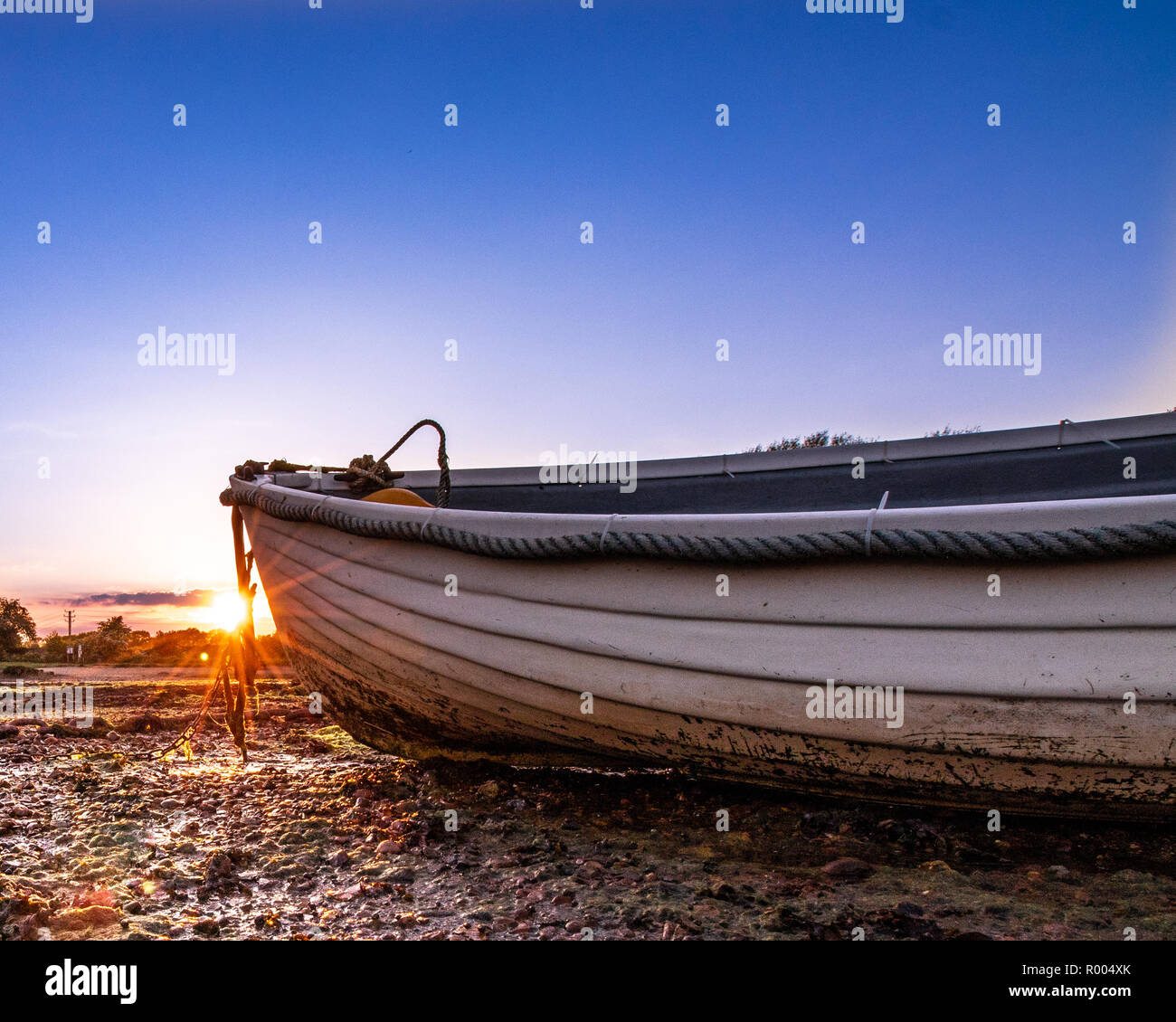 Un vecchio legno barca a remi a bassa marea con burst di Sun Foto Stock