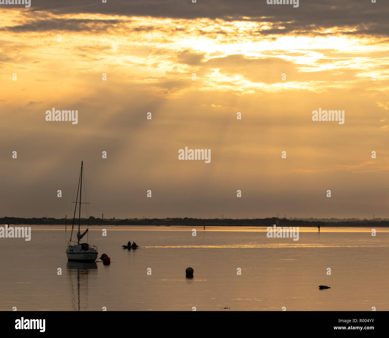 Una sola imbarcazione a vela sul mare calmo al tramonto con i raggi di luce provenienti attraverso le nuvole Foto Stock