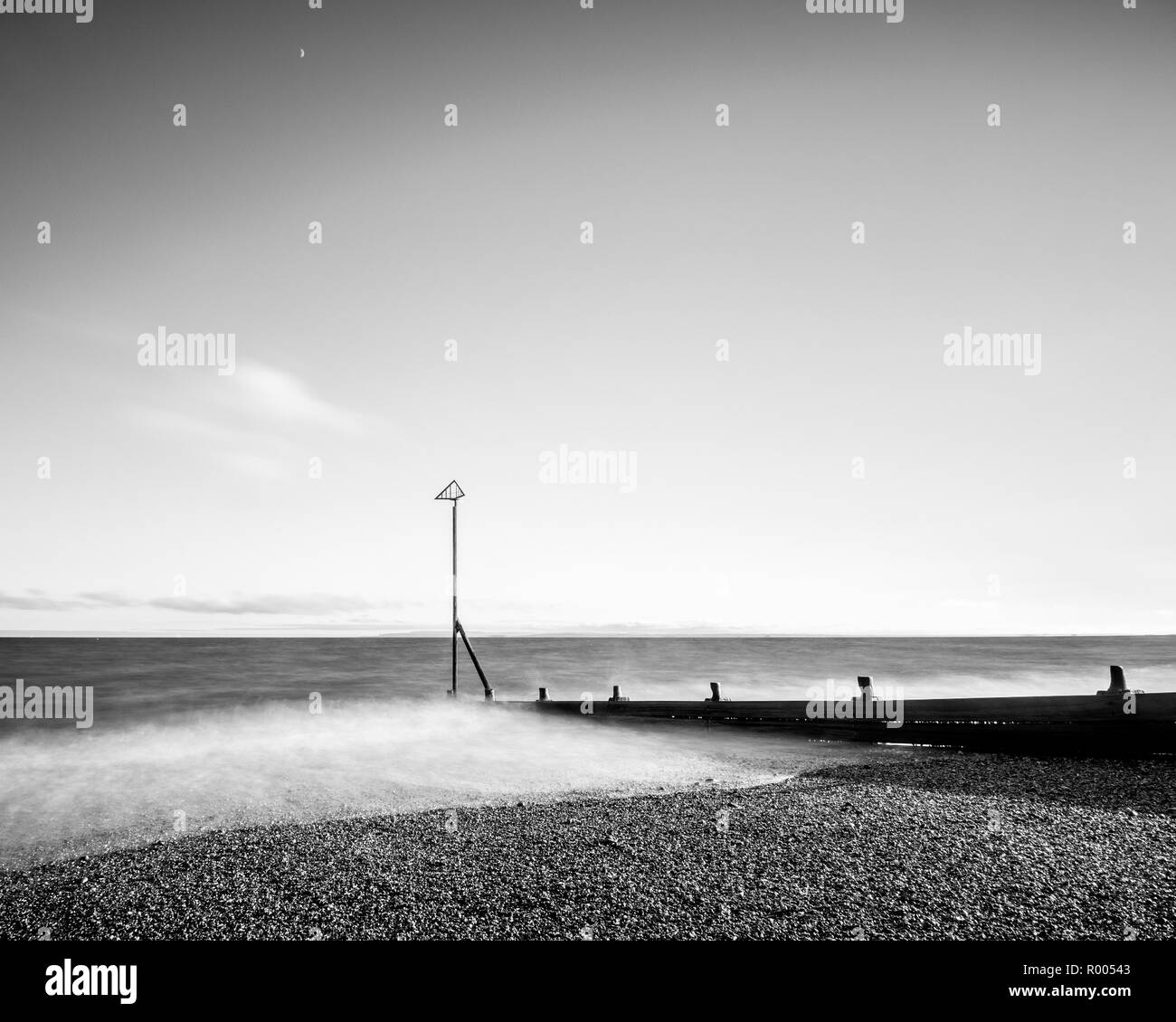 Un singolo marcatore sulla spiaggia o pennelli su una spiaggia con onde lavaggio delicatamente contro i ciottoli Foto Stock