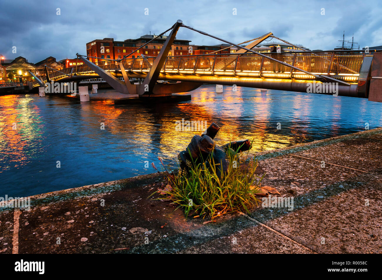 Illuminato il ponte pedonale a Dublino in Irlanda nel corso del fiume Liffey. Alberghi moderni in background Foto Stock