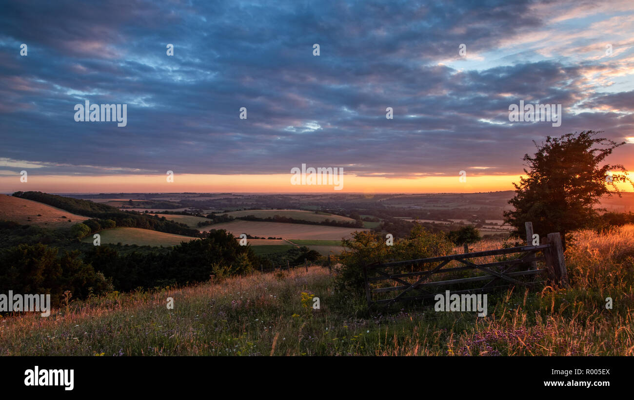 Campagna inglese e il tramonto con dolci colline e da un cancello in legno in primo piano Foto Stock
