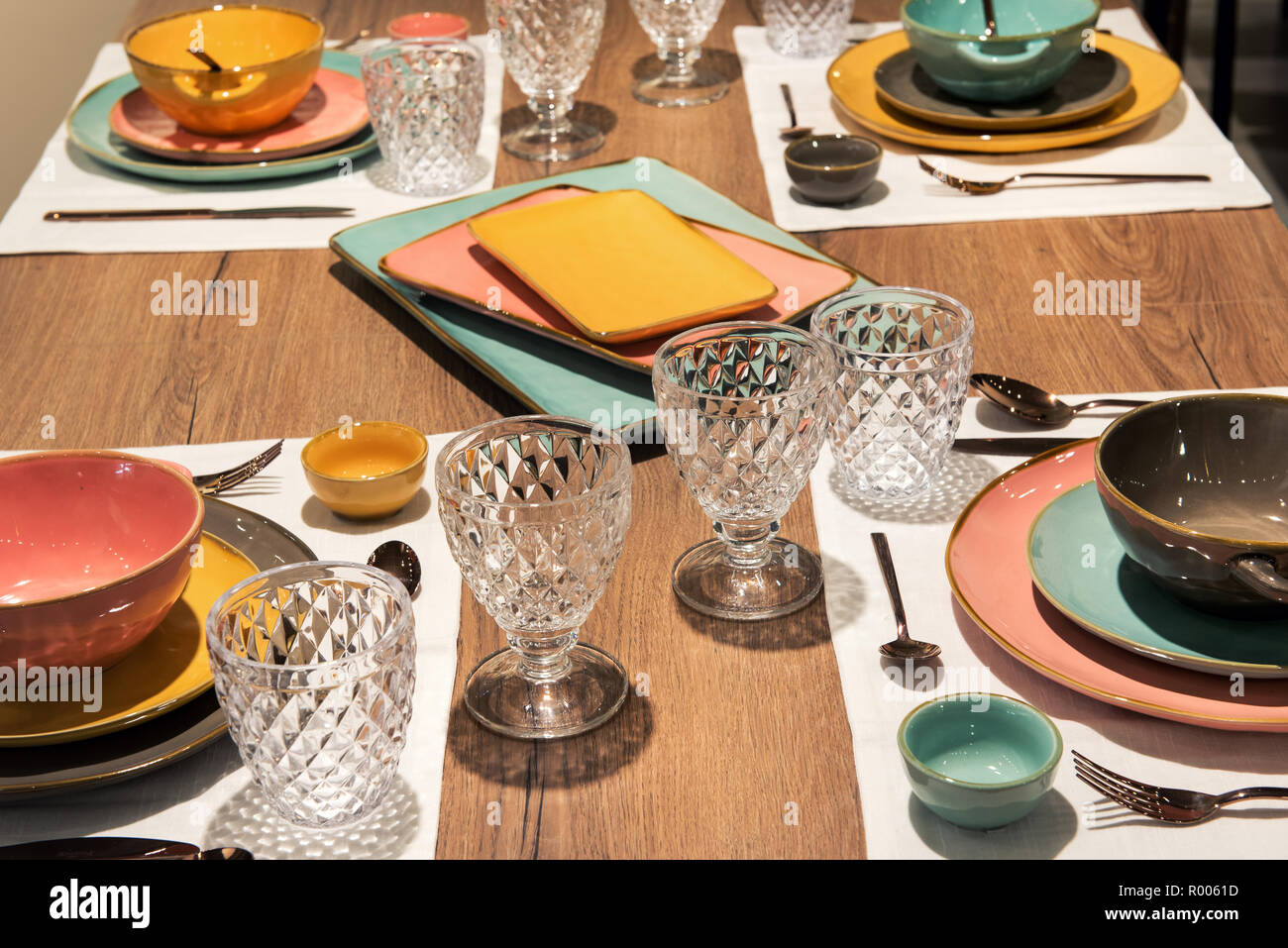 Mise en place tavolo per la cena con eleganti ceramiche colorate posateria e tagliare calici in vetro per una cena formale o catering evento Foto Stock