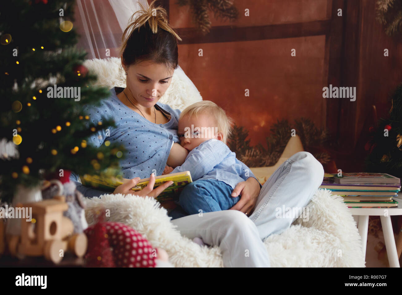 La madre di allattamento al seno il suo bambino figlio seduto in poltrona  accogliente vicino ad albero di Natale, inverno Foto stock - Alamy