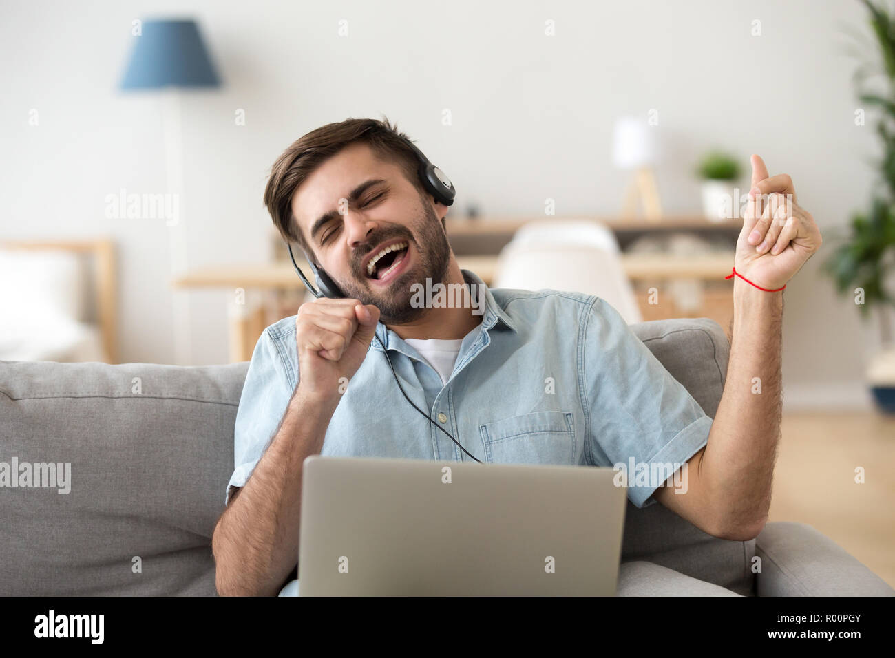 Uomo di cantare una canzone utilizzando laptop e cuffia Foto Stock