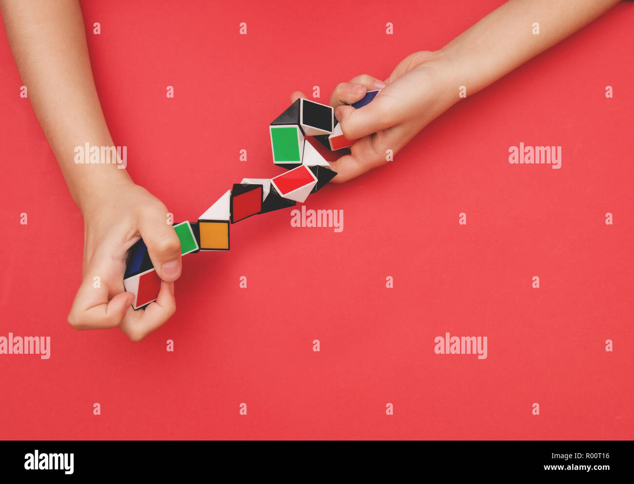 Colorato magic snake righello twist forme di puzzle in bambini con le mani in mano su sfondo rosso. Foto Stock