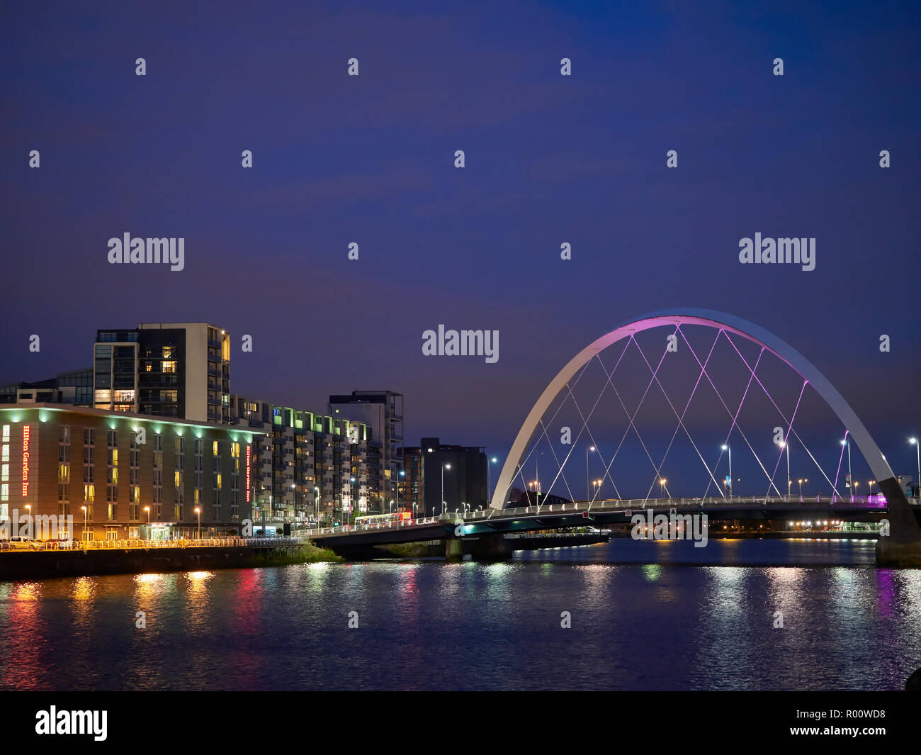 Guardando la Squinty Bridge di notte dal ponte di campane a Glasgow Waterfront District, con i riflessi di luce sull'acqua del fiume Clyd Foto Stock