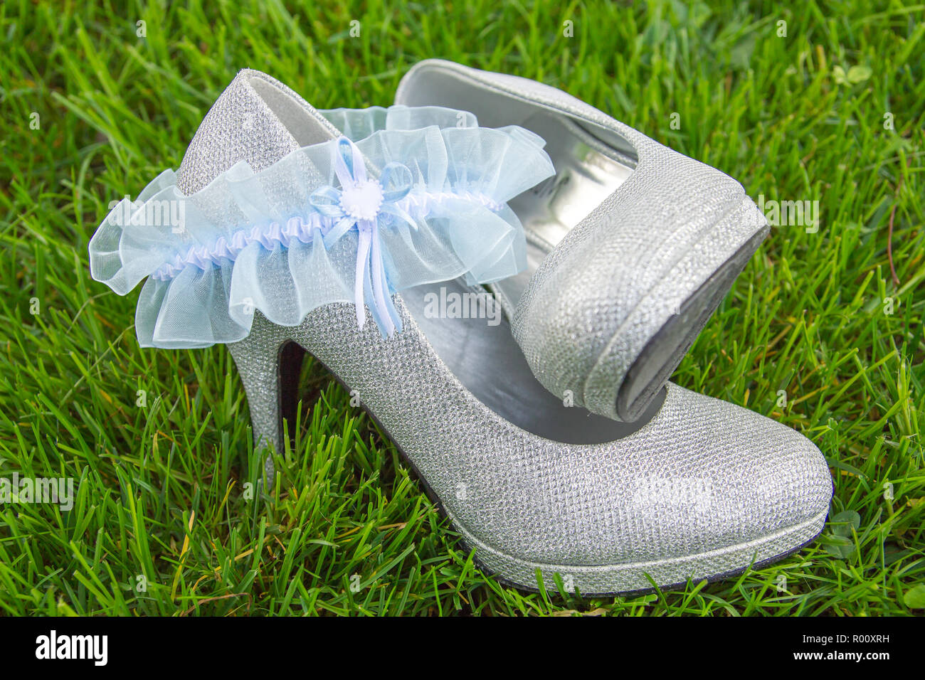 La luce blu giarrettiera del merletto disposti con argento tacco alto scarpe seduto in erba Foto Stock