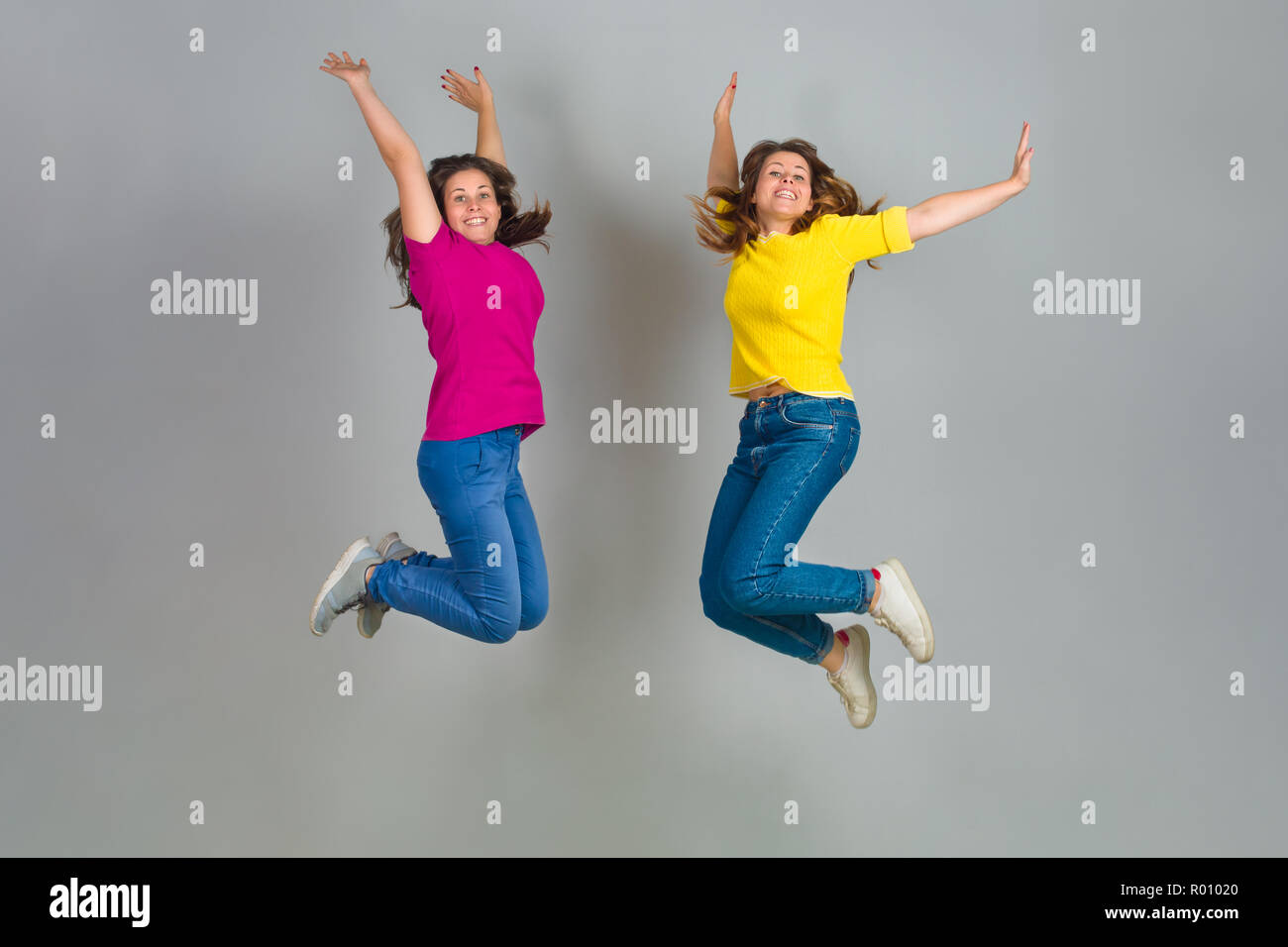 Due sorella gemella saltando su sfondo grigio Foto Stock