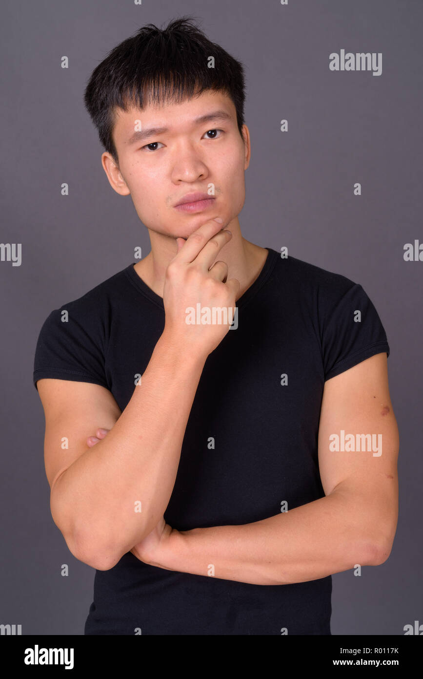 Studio shot del giovane uomo cinese contro lo sfondo grigio Foto Stock