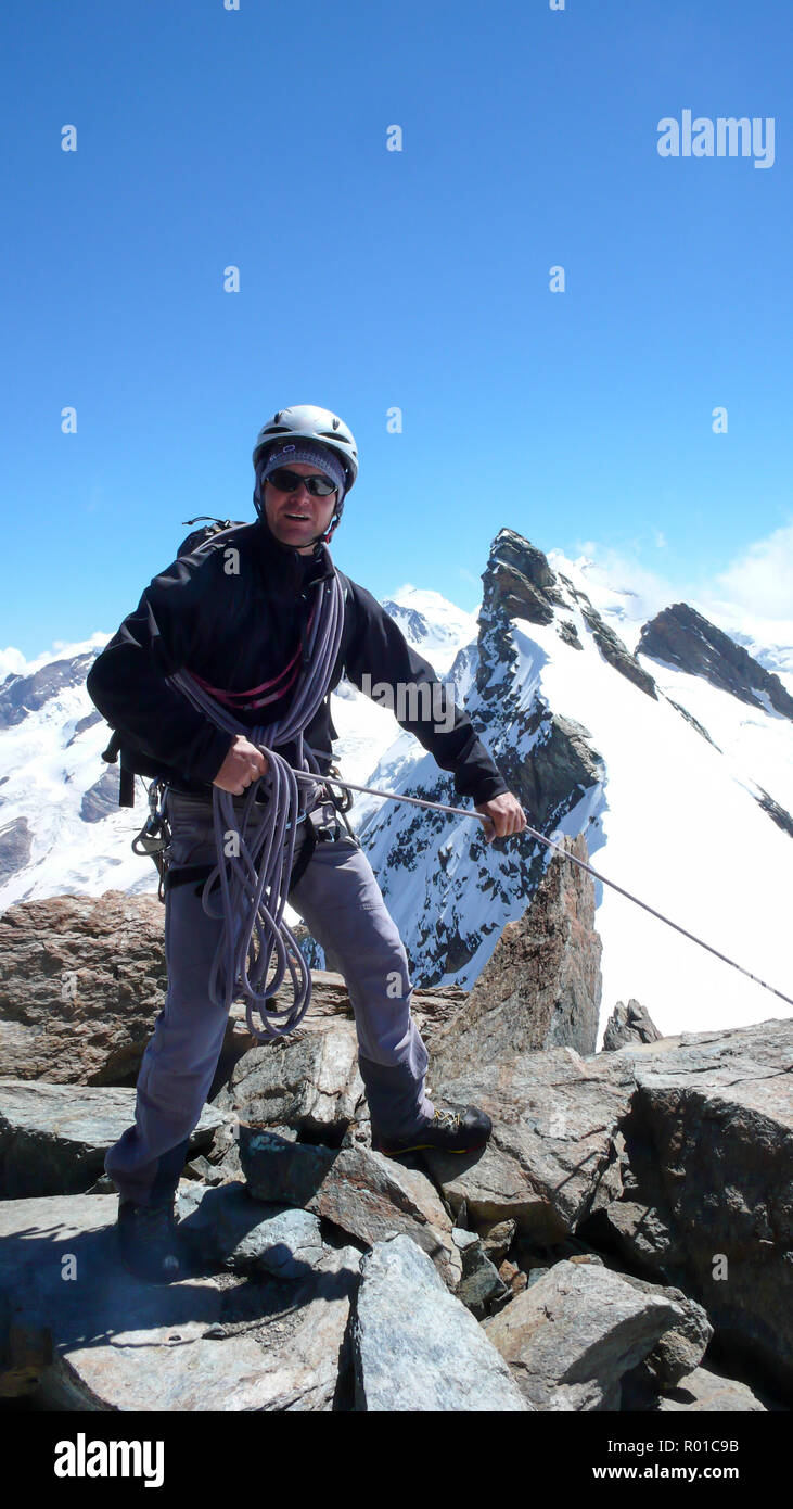 Guida di montagna in piedi su una roccia a picco di montagna e tirando un client su una fune con un fantastico paesaggio di montagna delle Alpi Svizzere dietro di lui Foto Stock
