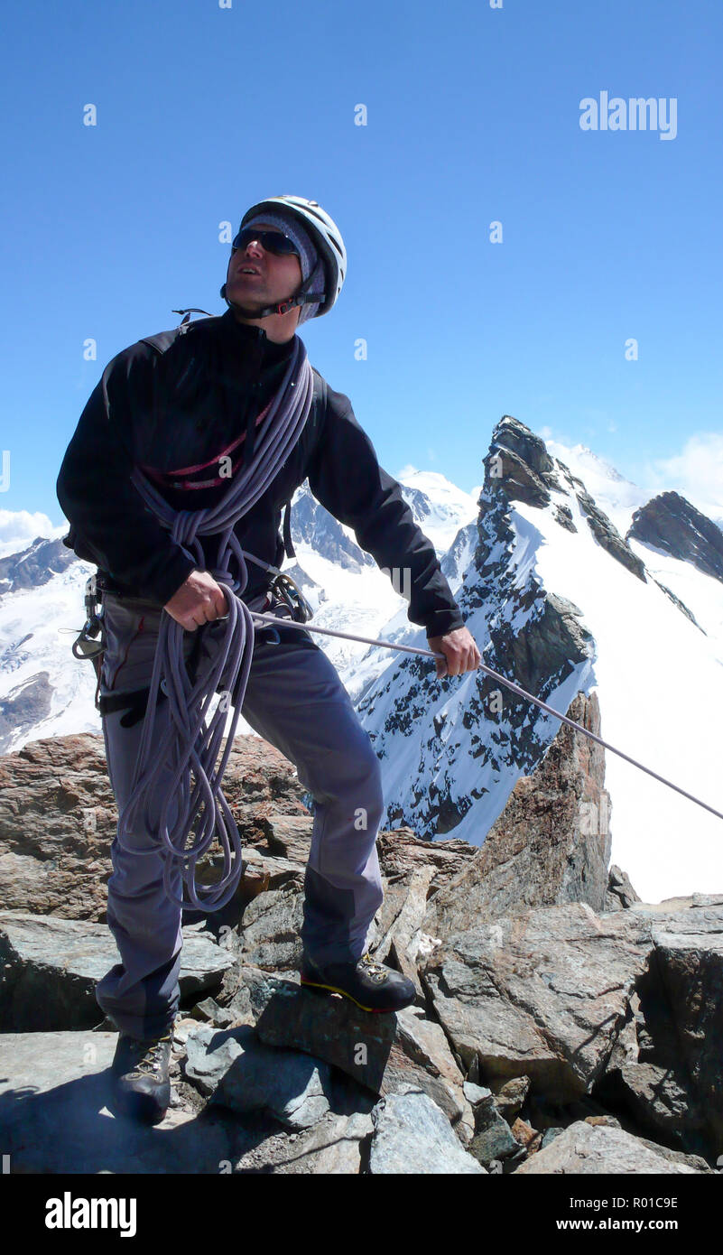 Guida di montagna in piedi su una roccia a picco di montagna e tirando un client su una fune con un fantastico paesaggio di montagna delle Alpi Svizzere dietro di lui Foto Stock