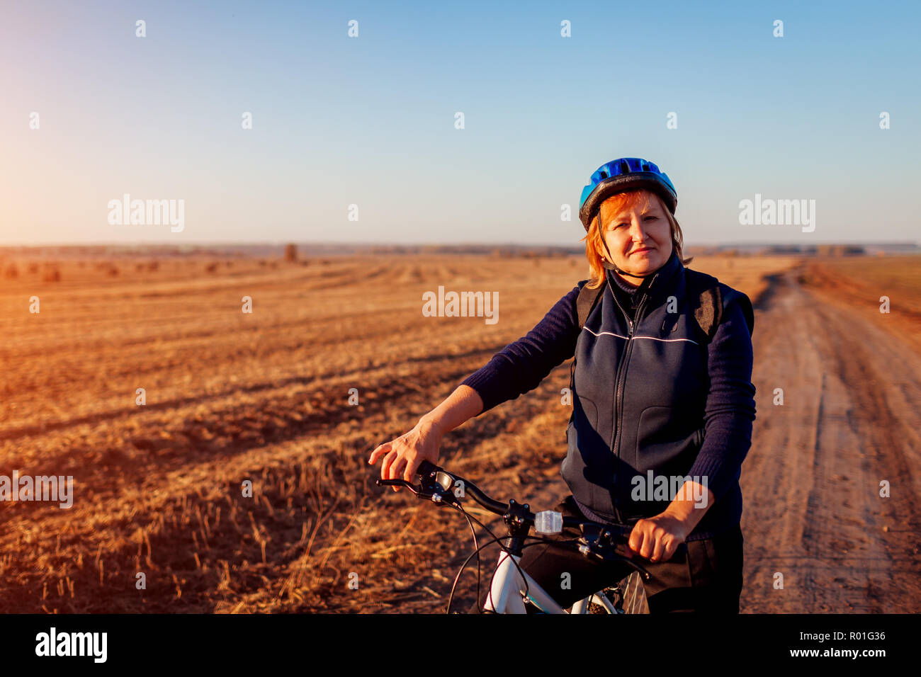 Donna di mezza età ciclista di equitazione in campo d'autunno al tramonto. Senior sportive godendo di hobby. Uno stile di vita sano Foto Stock