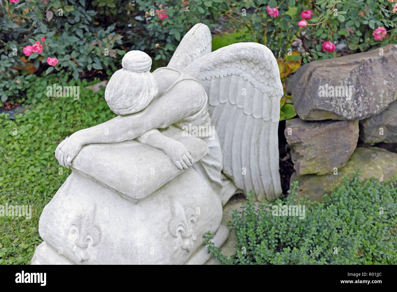 Un giardino statua di pietra di un Angelo seduto appoggiato su di una roccia. Essa può essere vista come il pianto, dorme, o esaurito. Foto Stock
