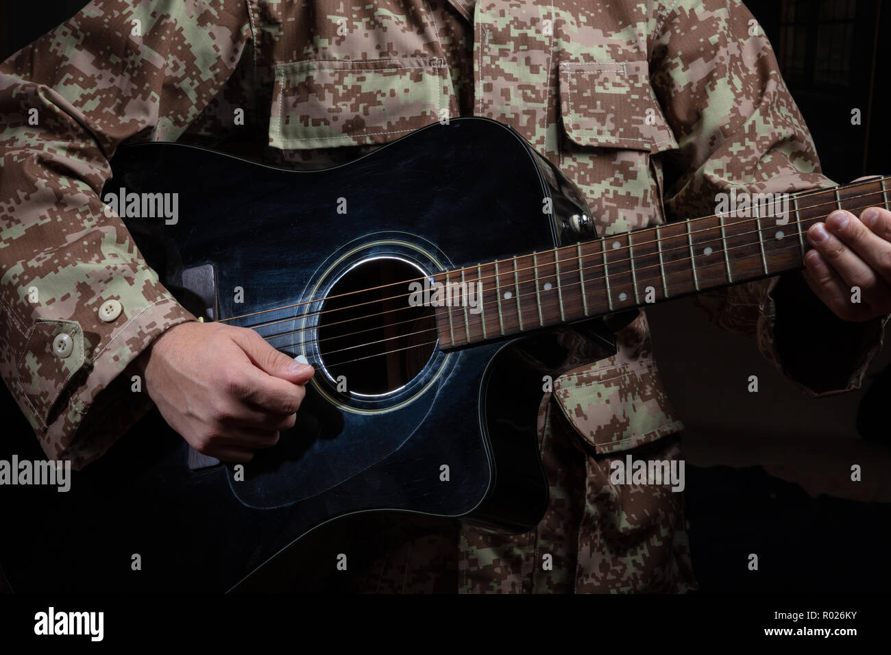 Giovane uomo in uniforme militare a suonare la chitarra, vista ravvicinata, sfondo scuro Foto Stock